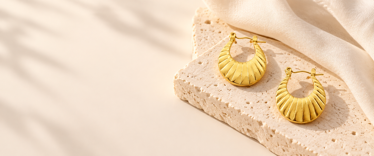 Golden textured hoop earrings styled on warm stone and ivory fabric